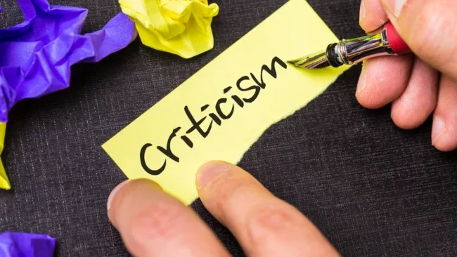 Person writing the word 'criticism' onto scrap paper